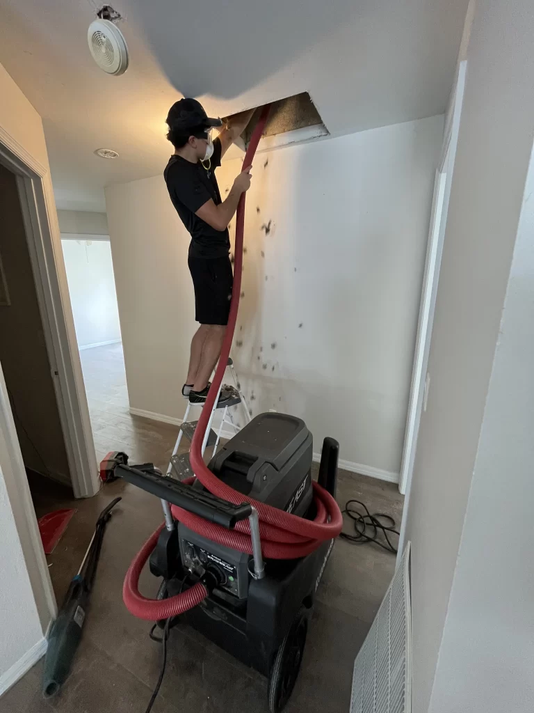 Worker using an air duct cleaning machine and hose to remove dust in the air duct of a ceiling in a residential home in Orlando, FL.